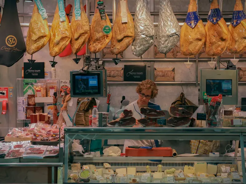 Mostrador de un deli con jamones colgados, quesos en la vitrina y una balanza